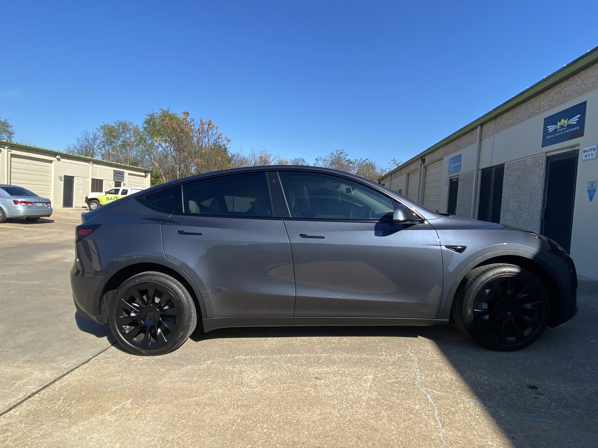 Gray Tesla Model Y parked outside a building with black wheels and tinted windows.