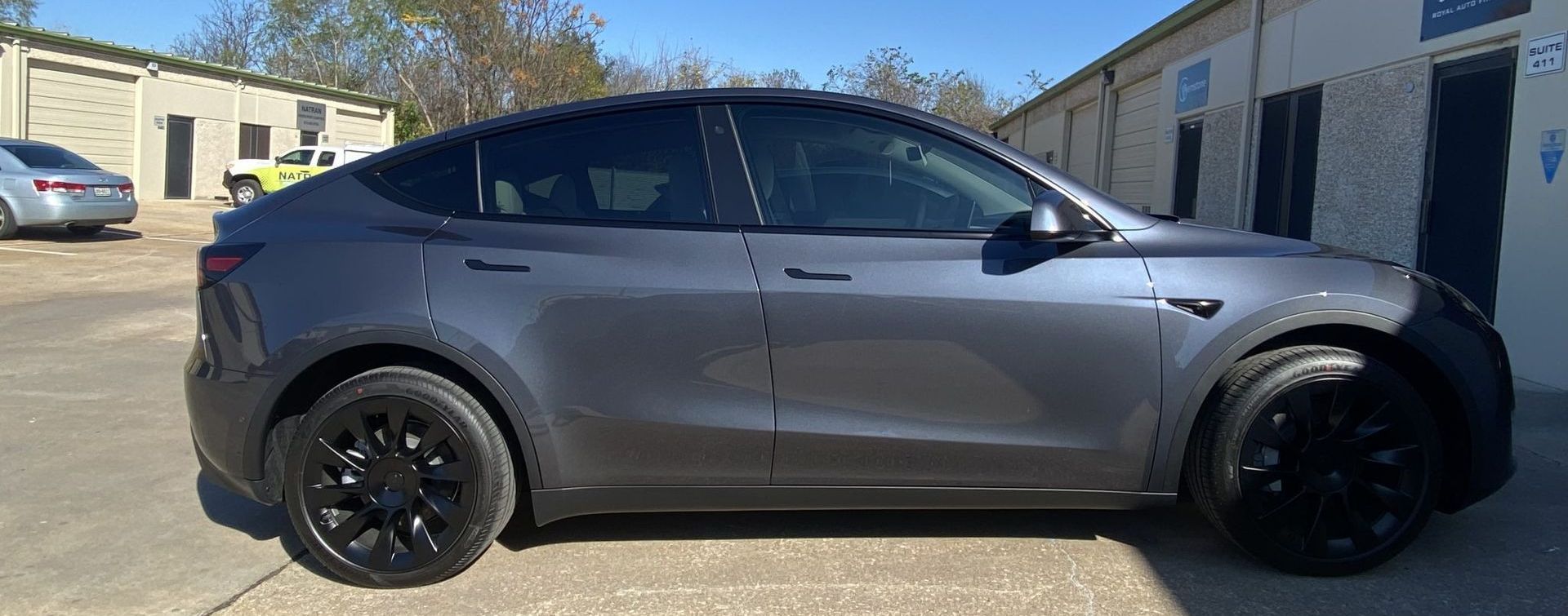 Gray Tesla Y model car with black rims parked outside a building.