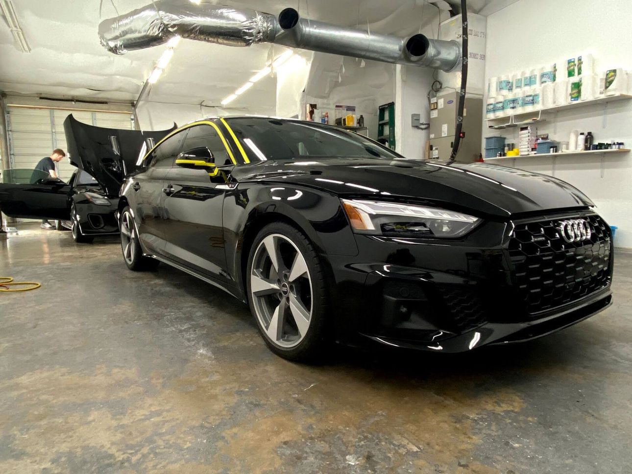 Black Audi sedan in a shop with open hood, being worked on.