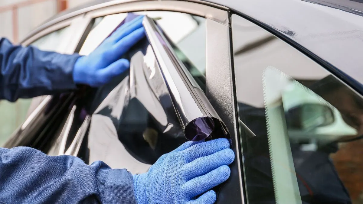 Person wearing blue gloves applying tinted film to a car window.