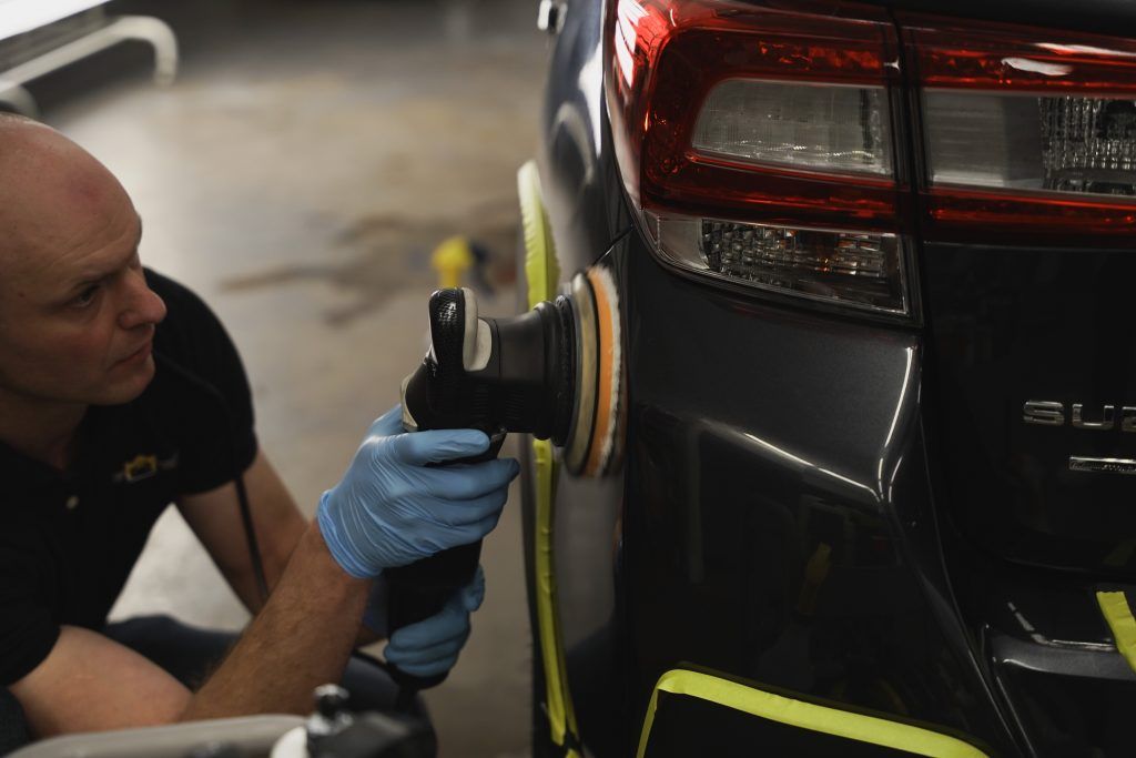 Man polishing a car bumper with a machine in a garage.