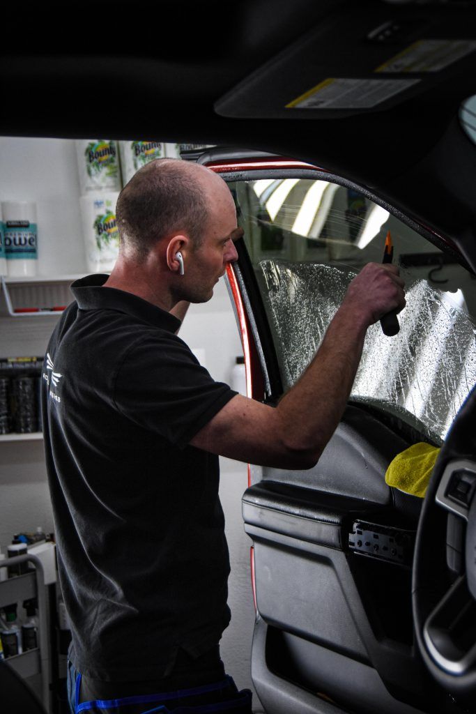 Man applying tint to a car window. He uses a tool with both hands. Interior shot.