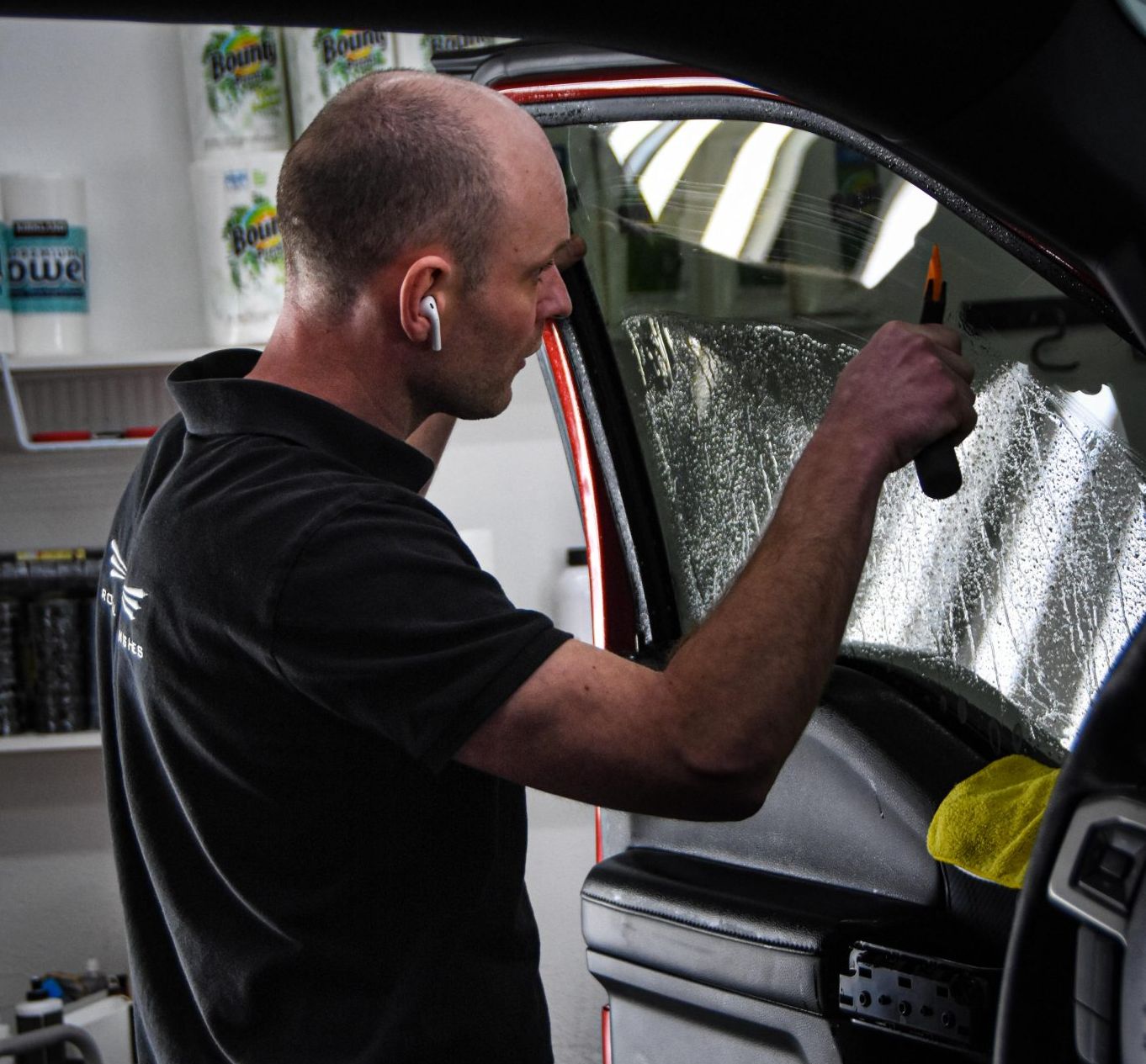 Man applying window tint to a car window, holding a tool, indoors.