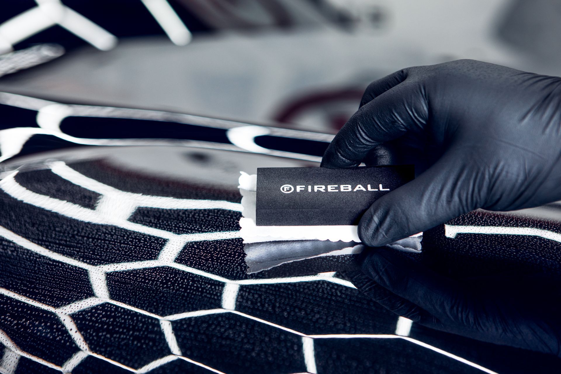 Gloved hand applying ceramic coating with applicator to a dark car hood. White hexagonal foam.