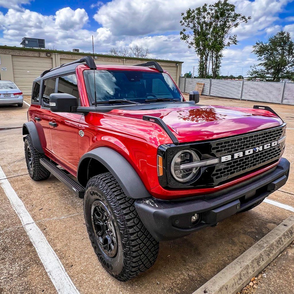 Red Ford Bronco parked in a lot, black wheels and trim, under a cloudy sky.