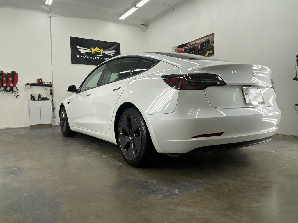 White Tesla sedan in a garage, angled rear view.
