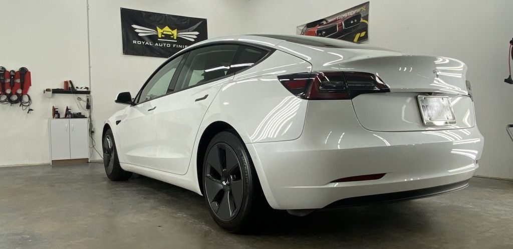 White Tesla Model 3 car parked inside a garage, next to cleaning supplies.