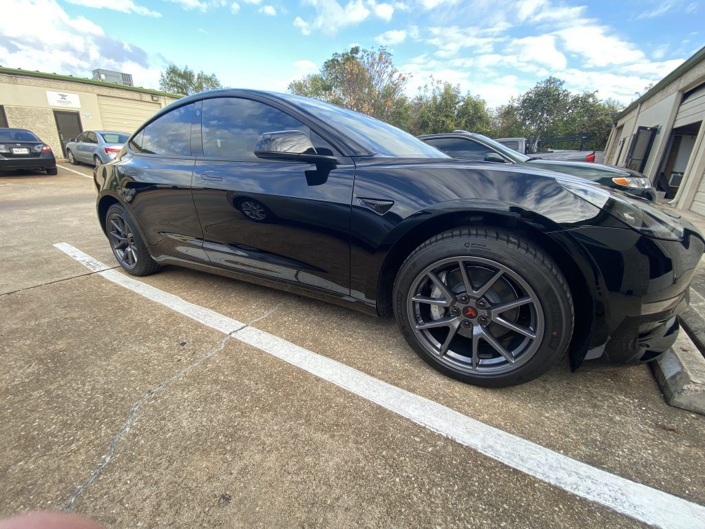 Black Tesla car parked on concrete, near a building, in daylight.