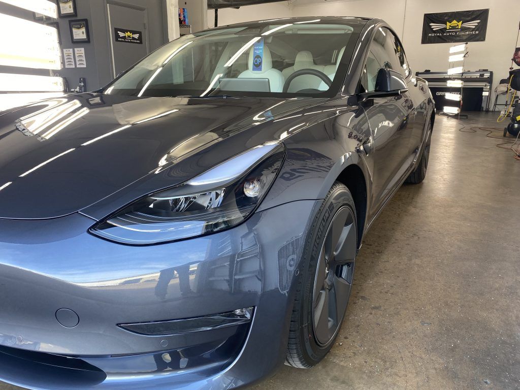 Gray Tesla Model 3 car parked inside a garage, with bright overhead lighting.