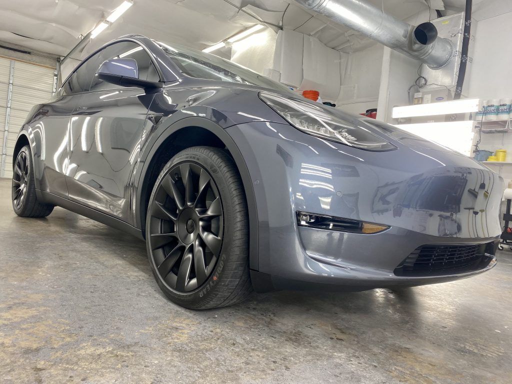 Gray Tesla Model Y car with black wheels in a garage.