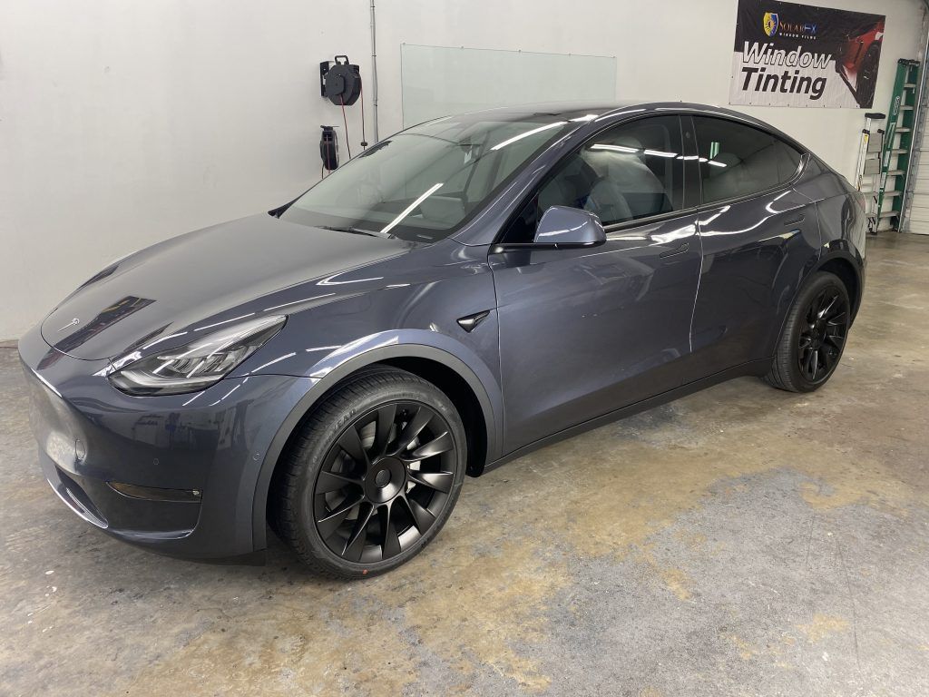A dark gray Tesla Model Y car with black wheels in a garage setting.