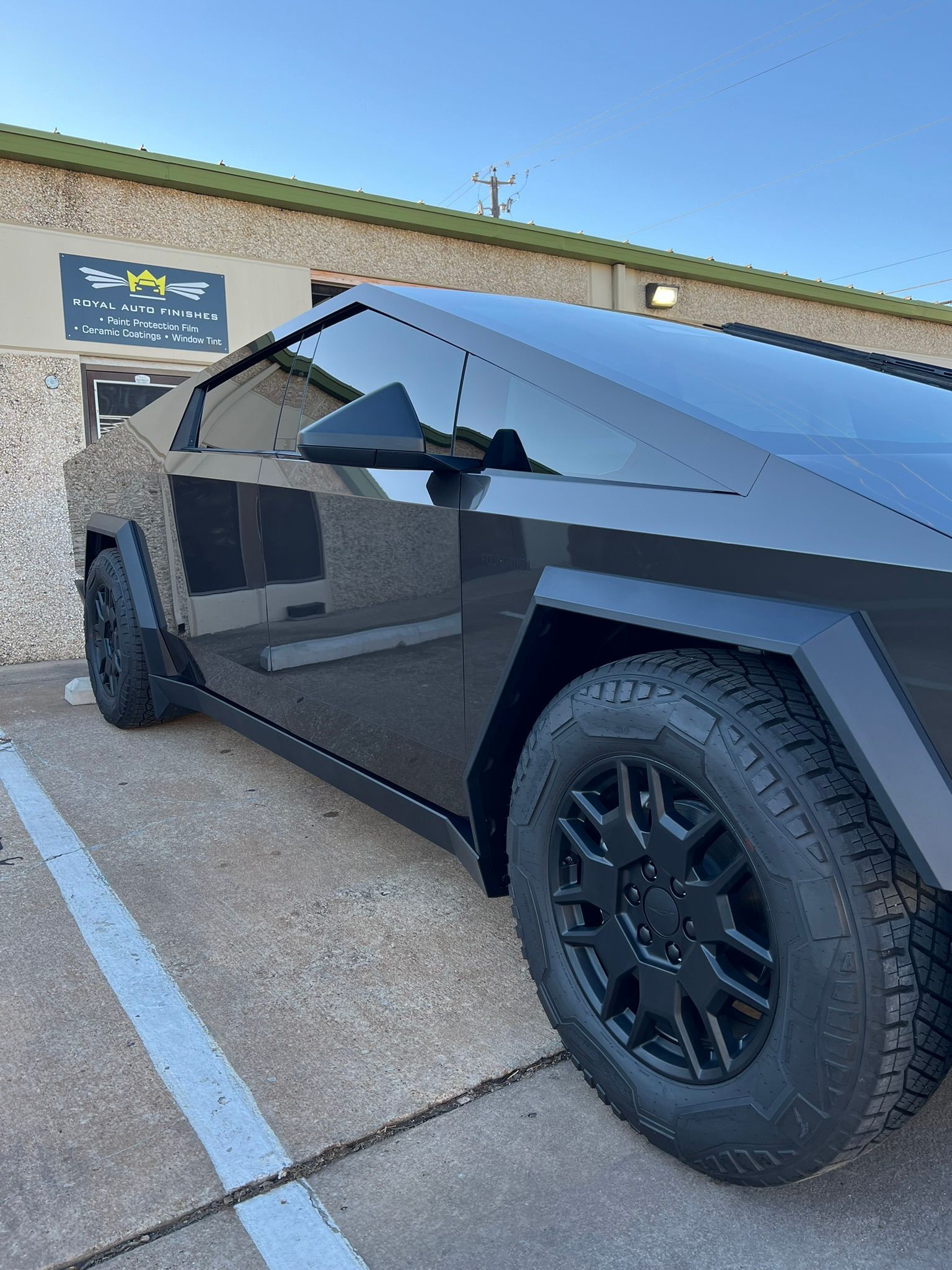Black Tesla Cybertruck parked outside a building with a blue sky background.