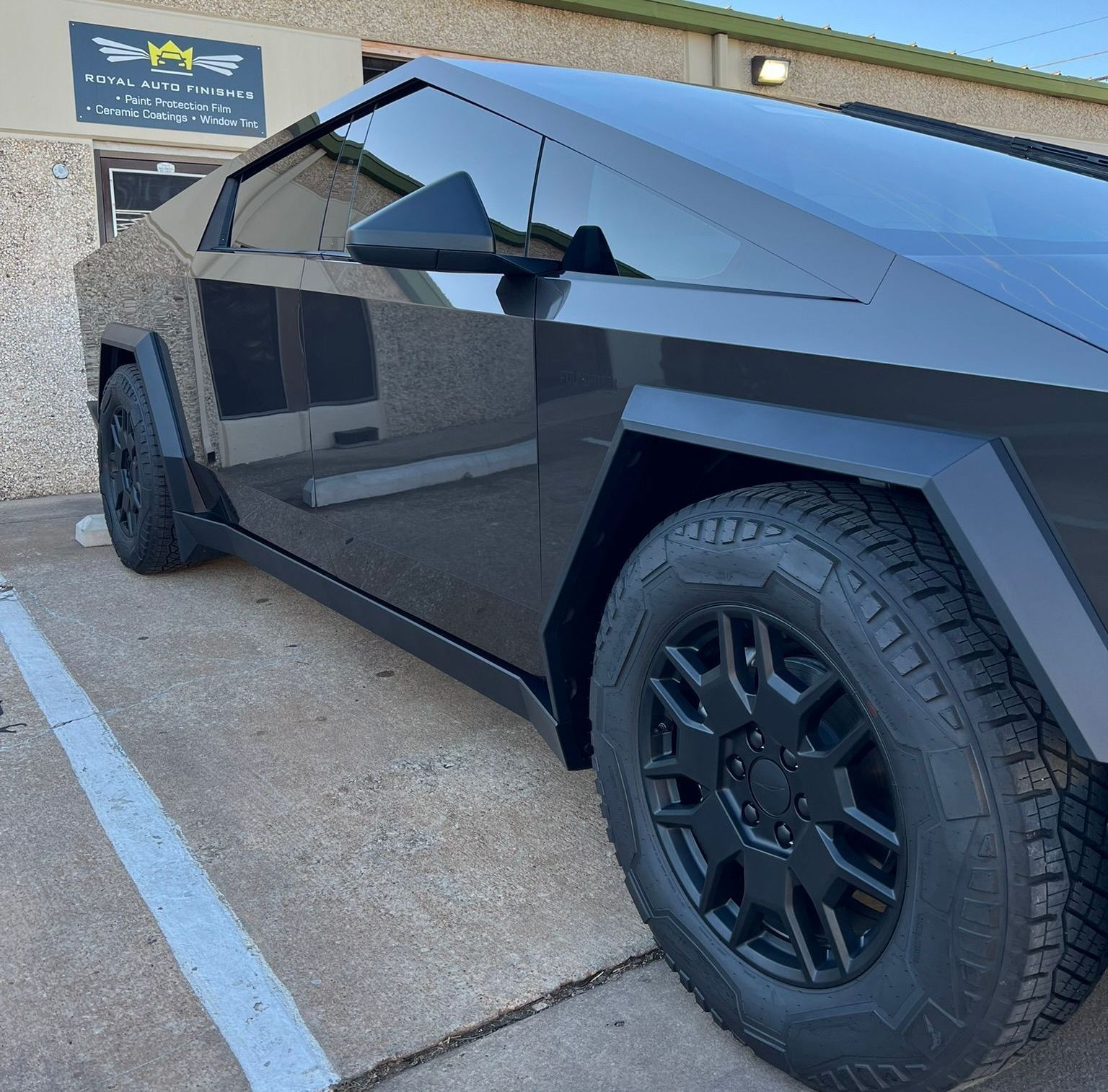 Black Tesla Cybertruck parked outside a building, angled view showing the front, side and tires.