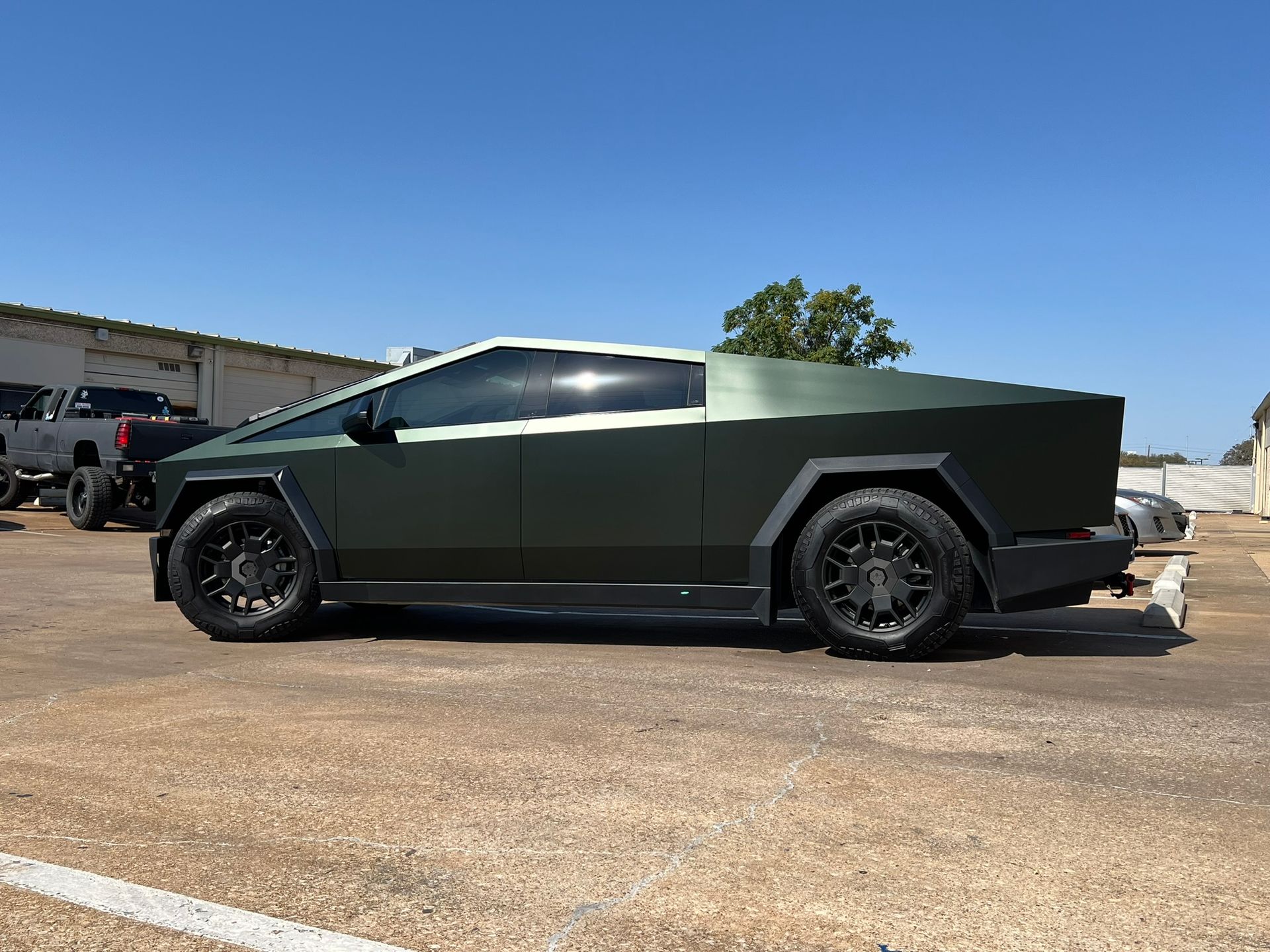 Dark green Tesla Cybertruck with black wheels parked outside on a sunny day.