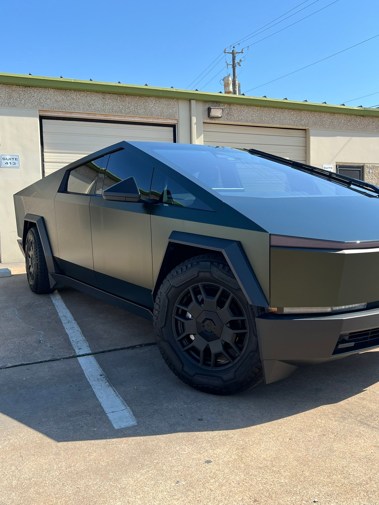 Matte black Tesla Cybertruck parked outside a building, in a parking space.
