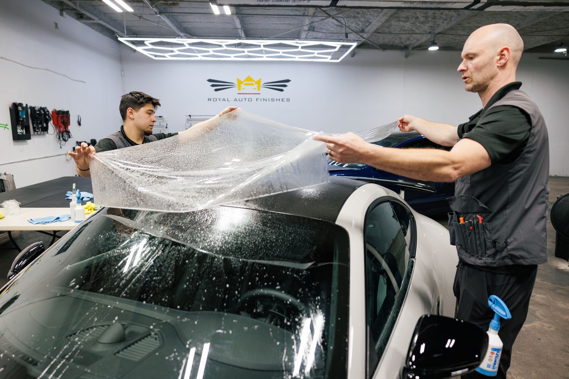 Two men applying protective film to a car roof inside a garage.