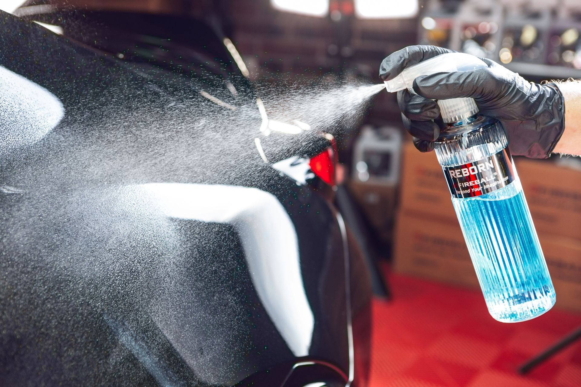 Black-gloved hand spraying blue liquid on a black car; detail of a car wash.