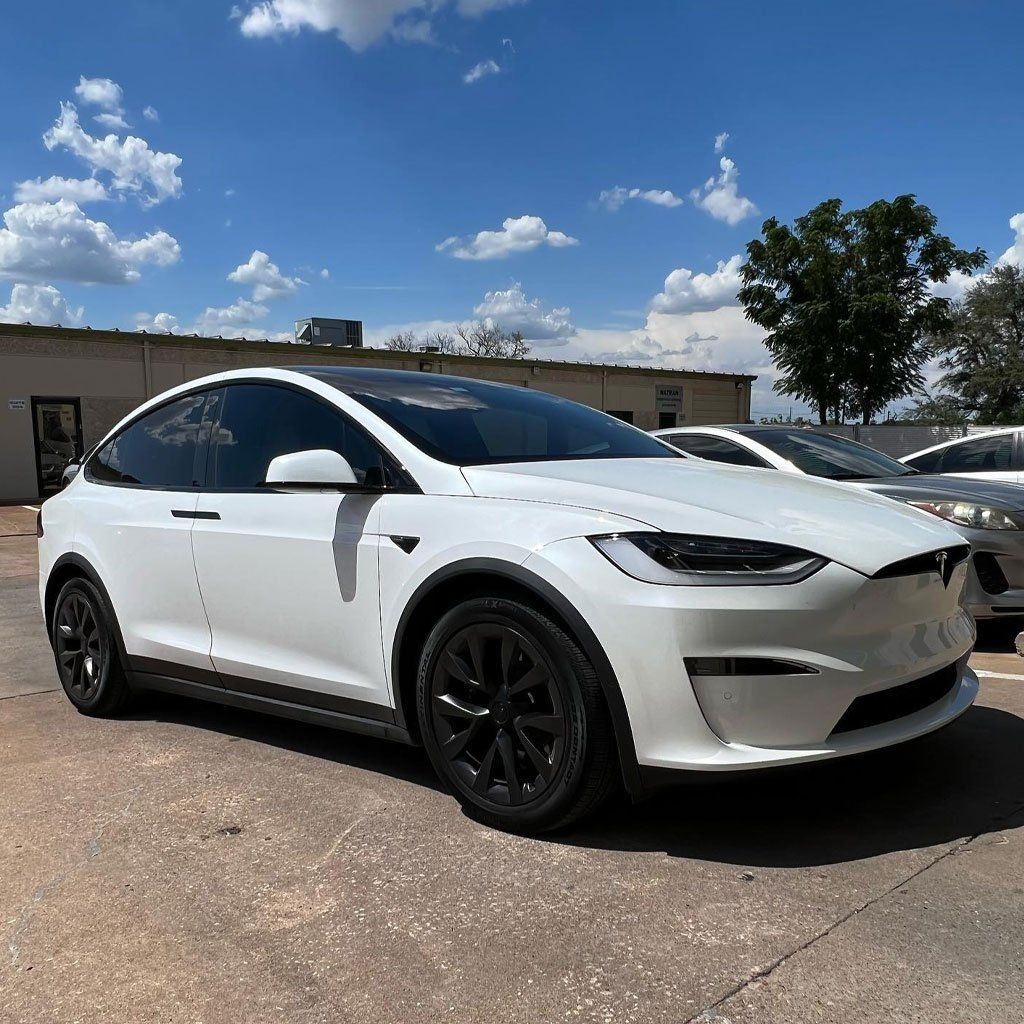 White Tesla Model X with black rims parked outdoors on a sunny day.