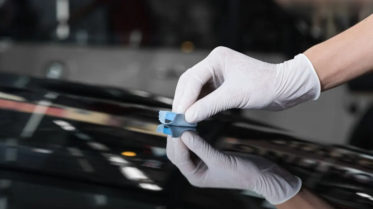 Gloved hand applying ceramic coating to a shiny black car surface with a blue applicator.