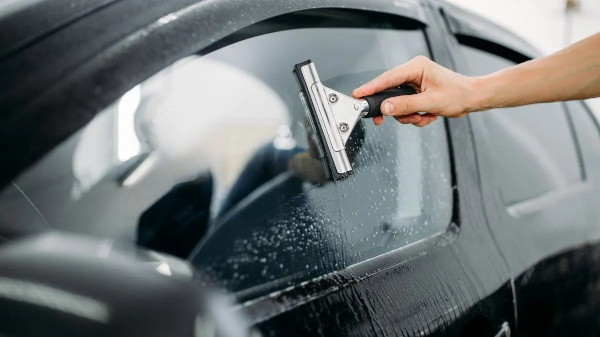 Person squeegeeing a car window. Water and interior of a black car are visible.
