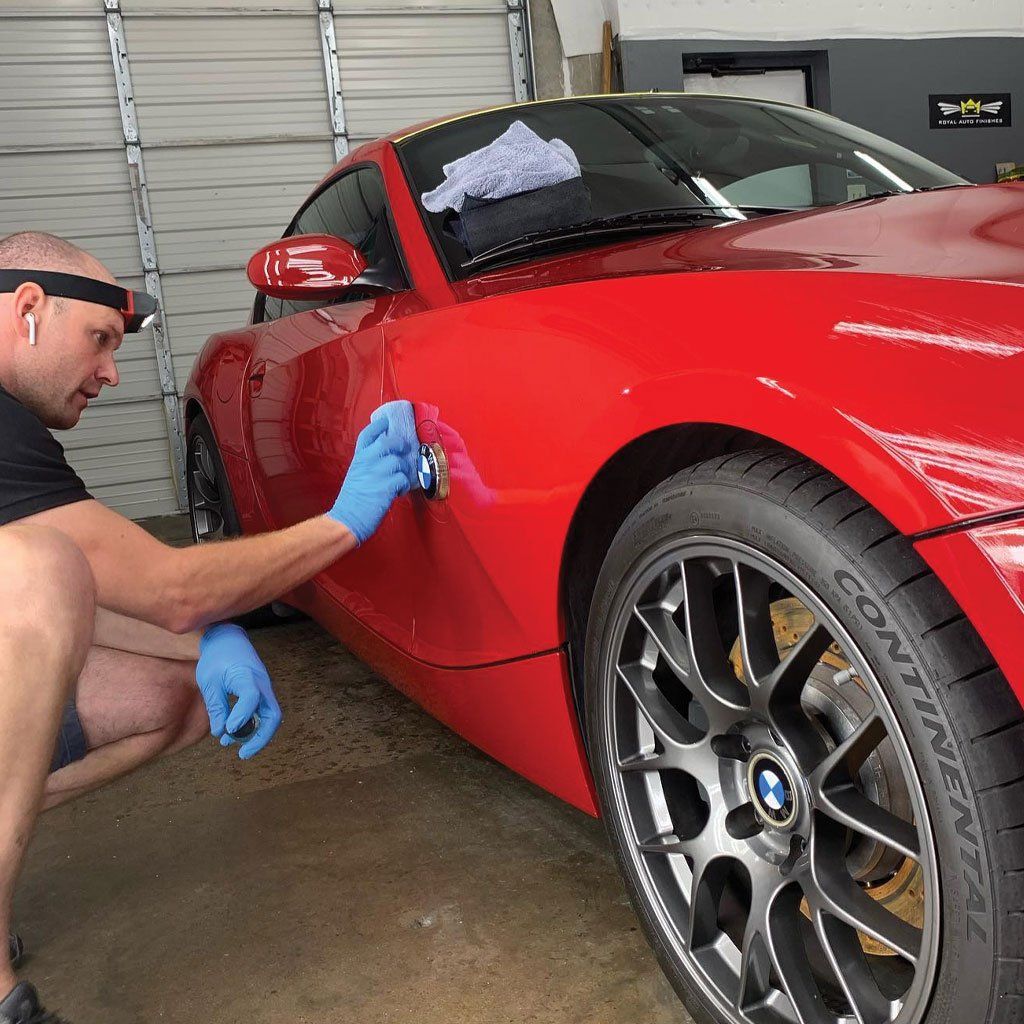 Man cleaning a red BMW car, wearing gloves and a headlamp in a garage.