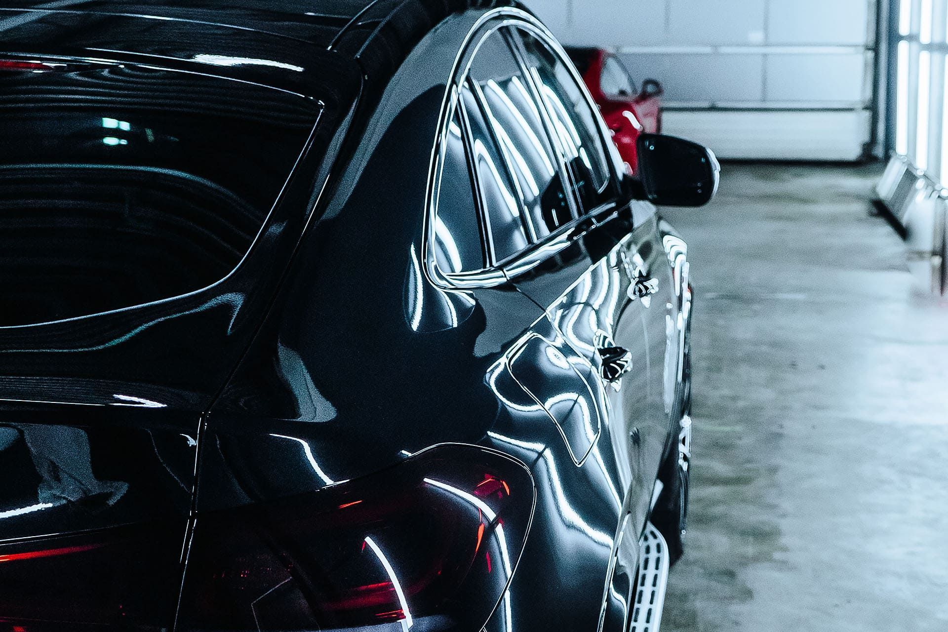 Black car in a brightly lit garage, reflecting the surroundings.