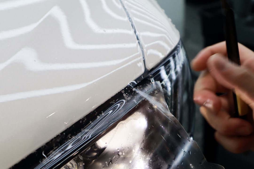 Applying a protective film to a white car. Close-up of hands using a squeegee to smooth out the film.