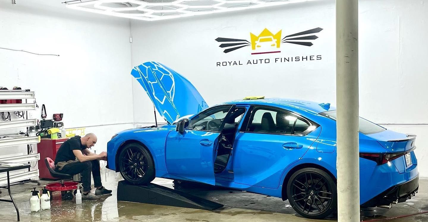 Man working on a bright blue car in a garage with logo 