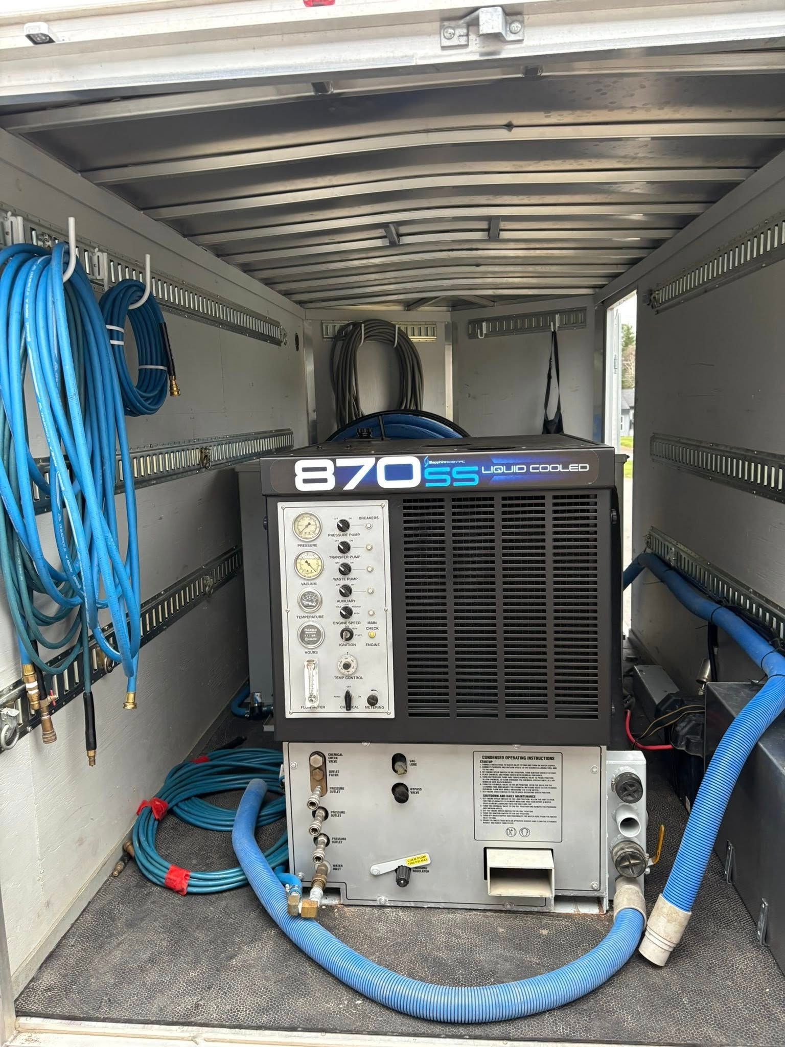 Intérieur d'un camion avec une machine de nettoyage de tapis, des tuyaux bleus et des étagères de rangement.