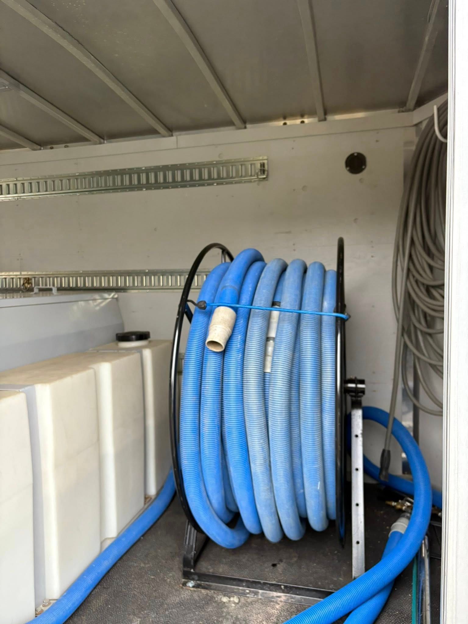 Un tuyau bleu enroulé sur un dévidoir à l'intérieur d'une camionnette blanche, près d'un réservoir d'eau.
