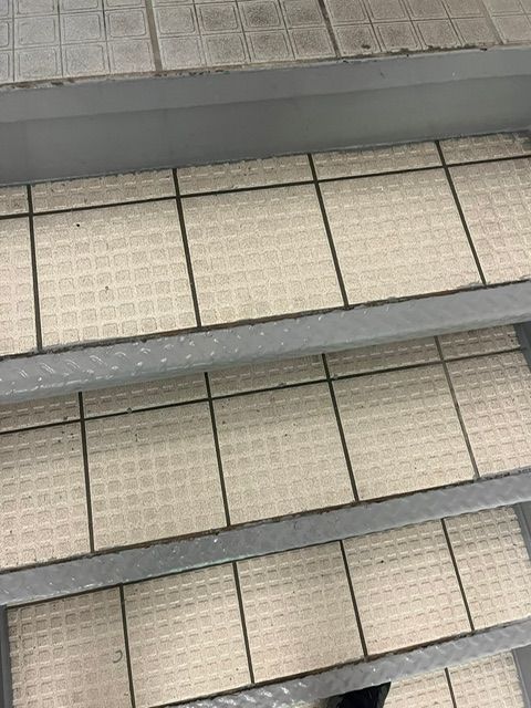 Escalier métallique avec marches carrelées blanc cassé et joints foncés, vu de dessus.