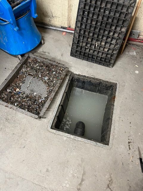 Point d'accès aux égouts ouvert avec eau stagnante, couvercle maintenu ouvert, débris visibles.