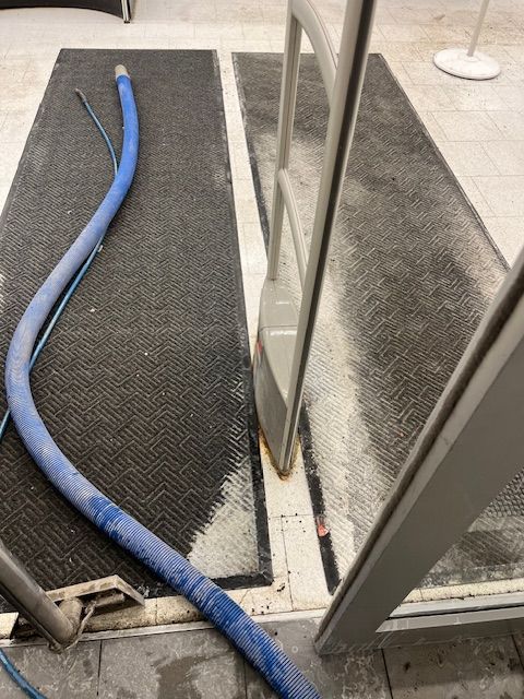 Tuyau bleu sur tapis noir devant le portail de sécurité du magasin, près de l'entrée.