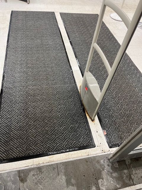 Portail de sécurité avec tapis à l'entrée d'un magasin. L'allée est équipée de tapis gris et d'une ligne de séparation blanche.