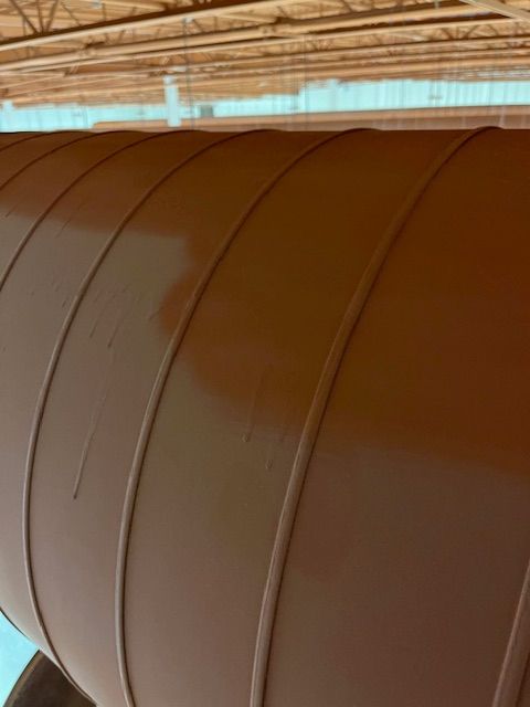 Des conduits cylindriques bruns courbent le plafond ; des supports de toit beiges sont visibles au-dessus.