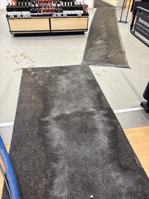 Tapis noirs sales sur un sol gris dans un magasin. Rayons avec des produits en arrière-plan.
