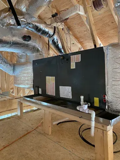Attic HVAC unit with insulated ducts and metal stand in unfinished attic space