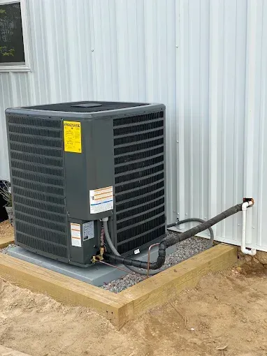 Outdoor HVAC unit beside a metal building, with a hose connected on a concrete pad