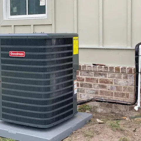 Outdoor Goodman air conditioner unit beside a house wall and brick foundation