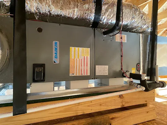 Gray HVAC furnace in a basement, with insulated ductwork, pipes, and wooden framing nearby