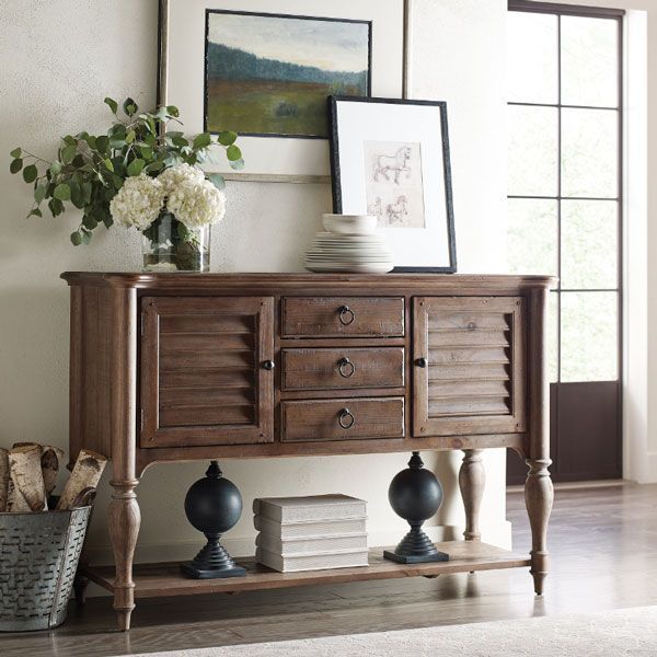 Wooden console table with flowers, framed art, books, and decorative objects in a bright entryway.