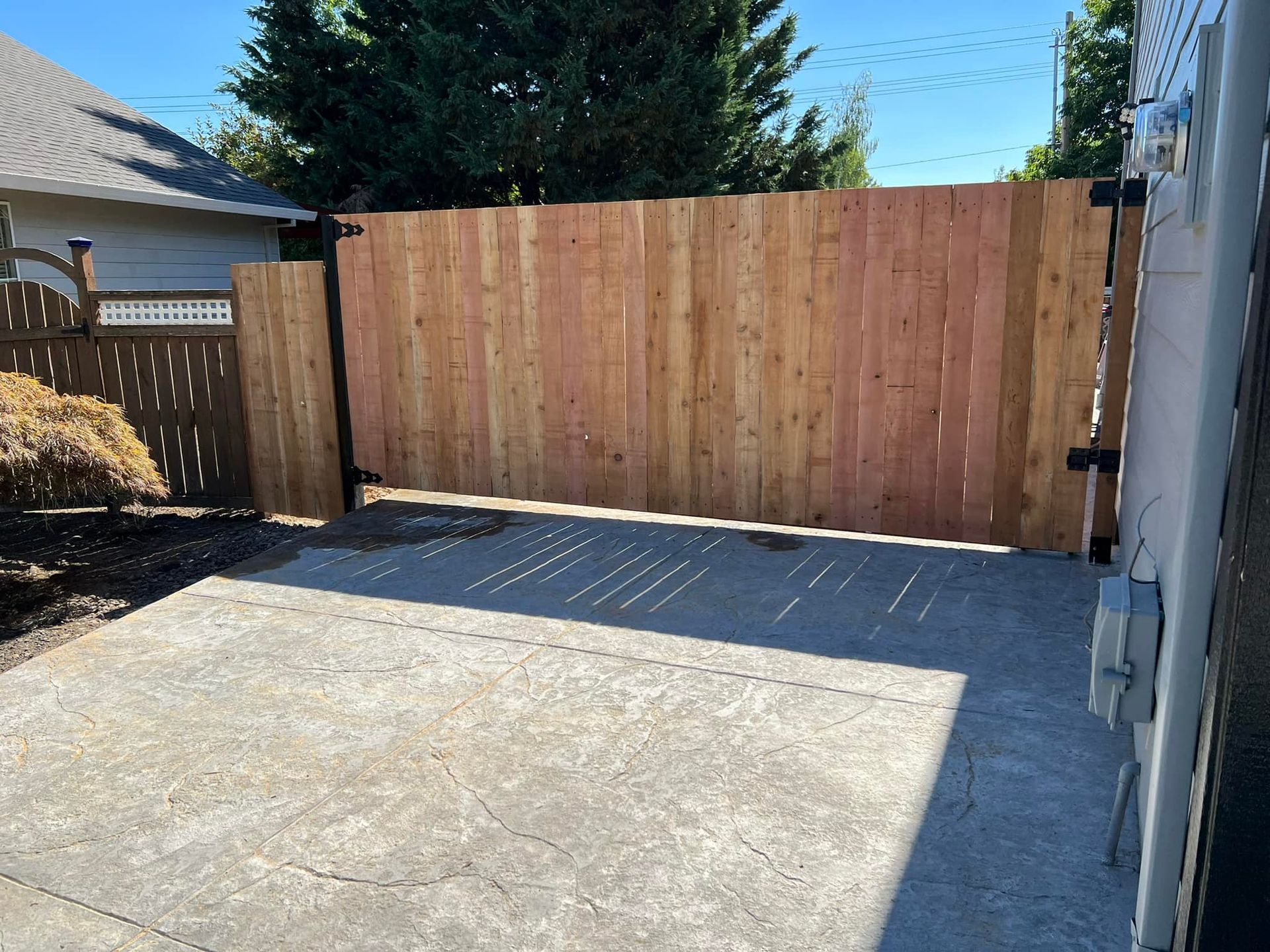 Wooden gate and fence on a concrete patio in front of a house on a sunny day.