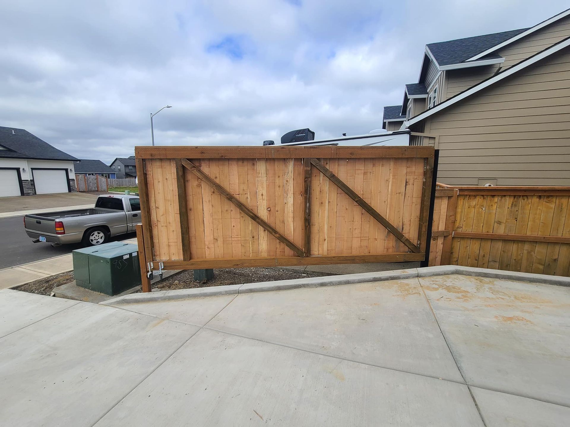 Wooden fence with diagonal supports, next to a concrete driveway and residential street.