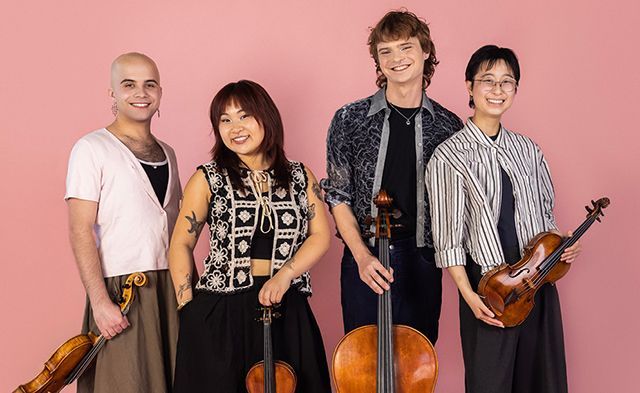 Four musicians sit together indoors, each holding a string instrument; they are dressed in formal, textured attire.