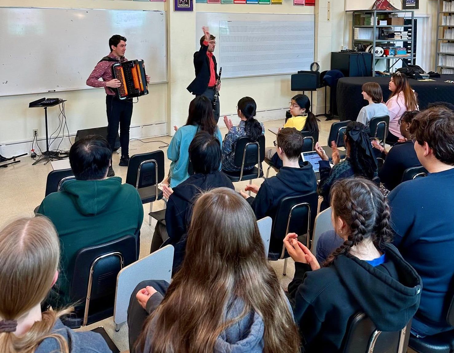 A group of people are sitting in a classroom watching a man play an accordion.