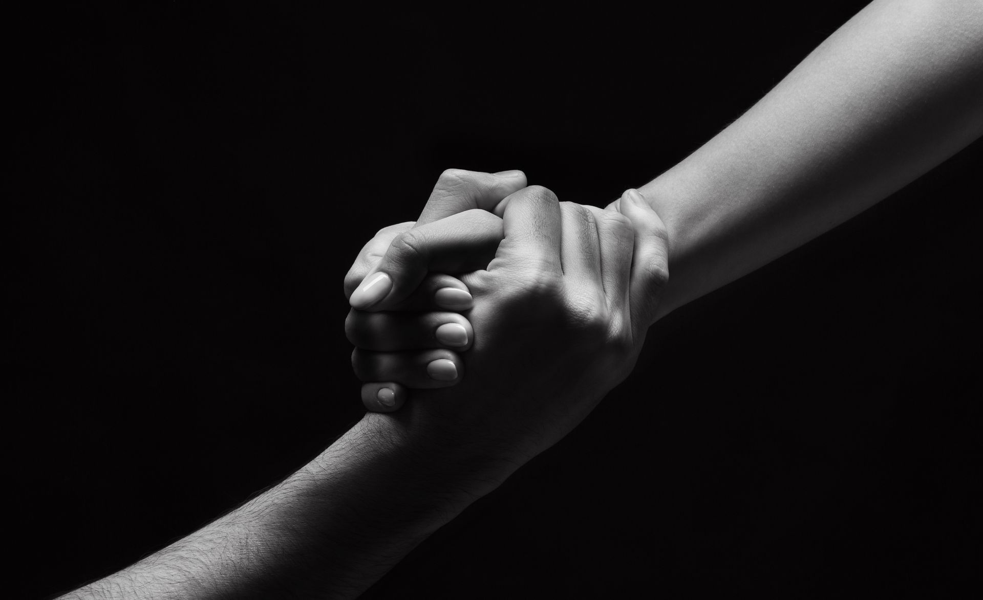 Two hands clasped together, reaching for each other. Black and white photo.