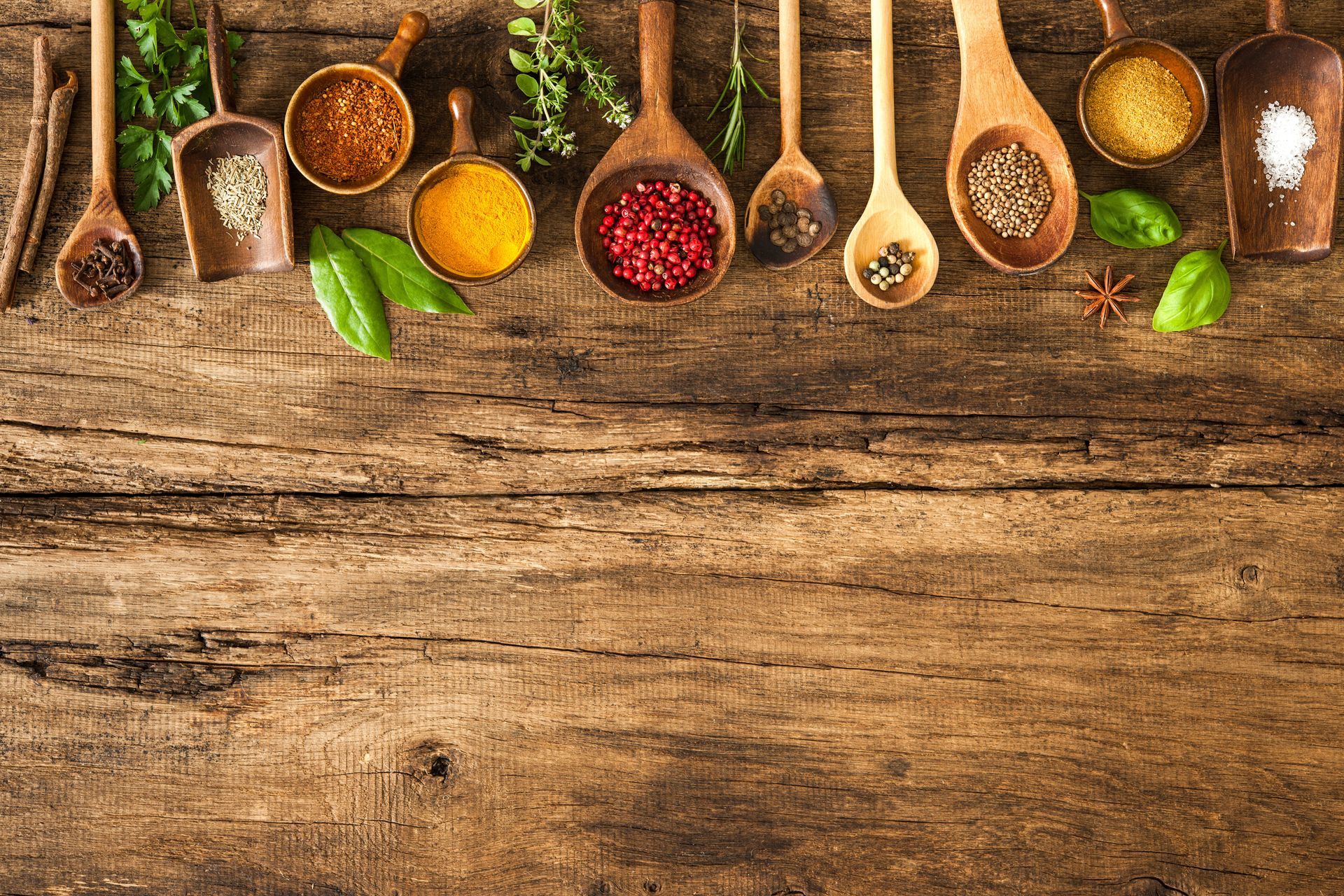Wooden spoons filled with various spices and herbs on a rustic wood table.