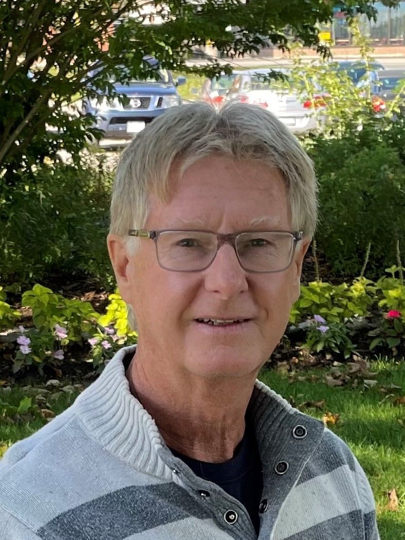 A man wearing glasses and a striped sweater is smiling for the camera.