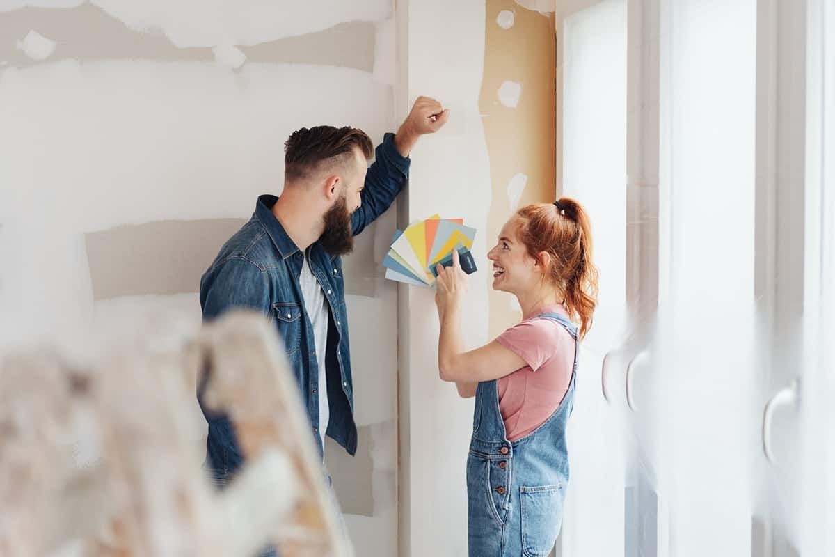 Two people standing in their home, comparing color swatches against an unfinished wall