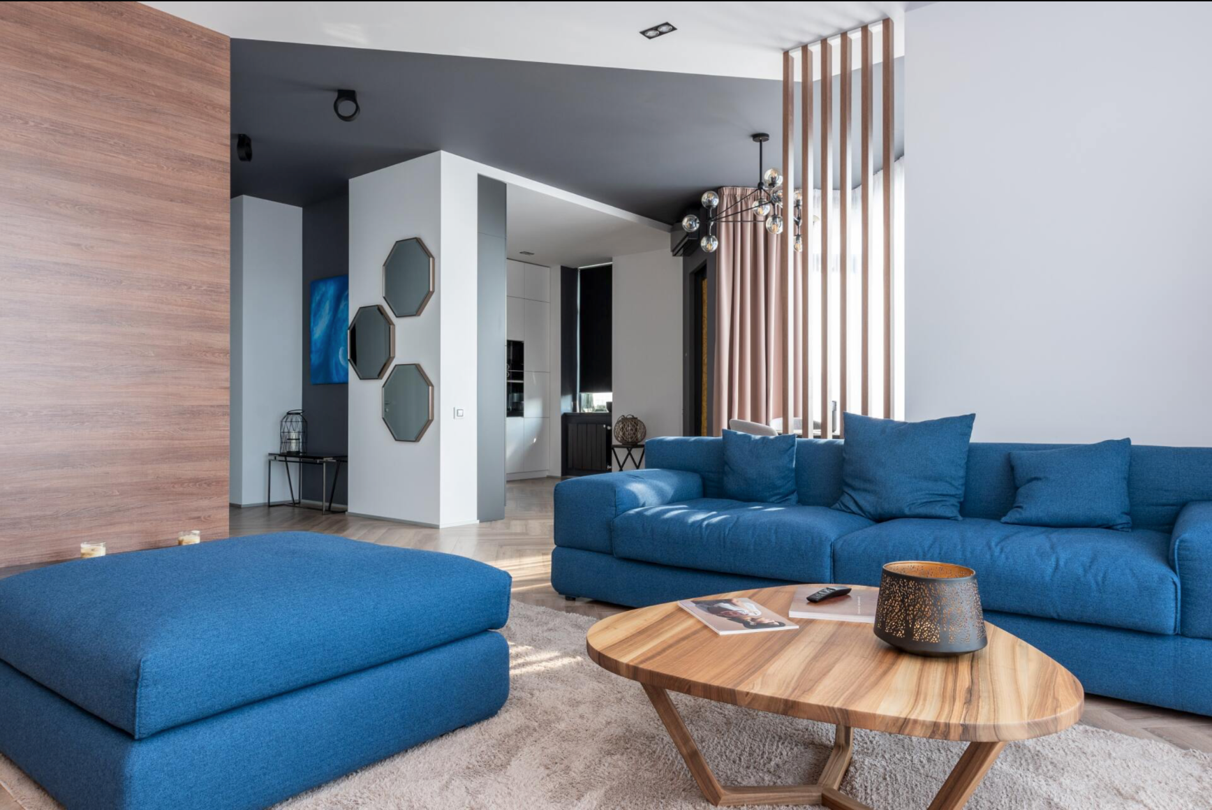 Modern living room with blue sectional, ottoman, wooden coffee table, and wood-paneled accent wall